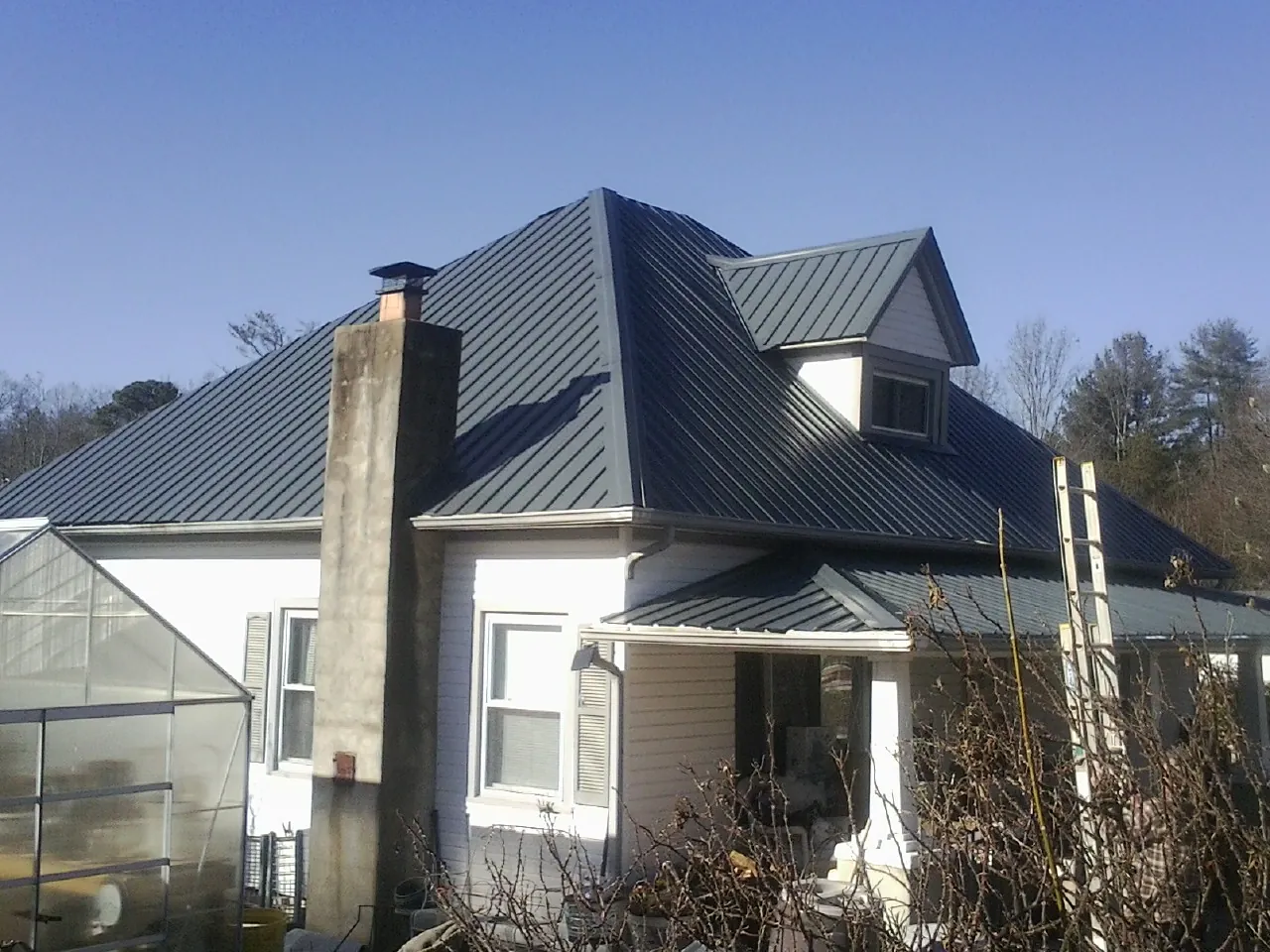 Dark blue standing seam metal roof on a white farmhouse with dormer — Slate & Tile Roof Repair by Roofing Brothers in Spottsville