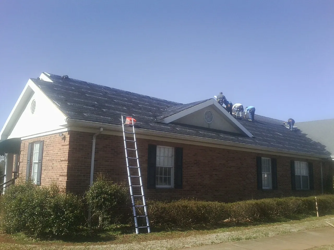 Crew tearing shingles off a brick ranch roof with a ladder set — Emergency Roof Repair work by our crew in Spottsville