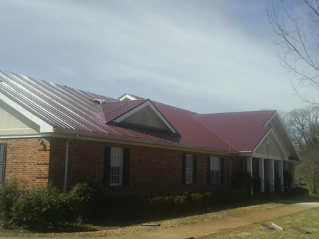 Red metal roof with gabled entries on a long brick building, from a Hail Damage Roof Repair job in Spottsville