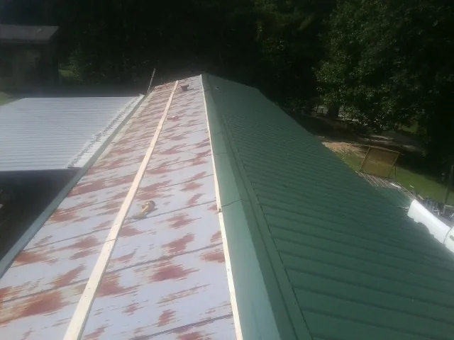 Old rusted panels beside newly installed green metal roofing — Wind Damage Roof Repair by Roofing Brothers in Spottsville