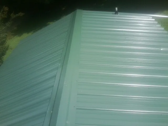New green metal panels meeting at the ridge of a roof — Flat Roof Repair work by our crew in Spottsville