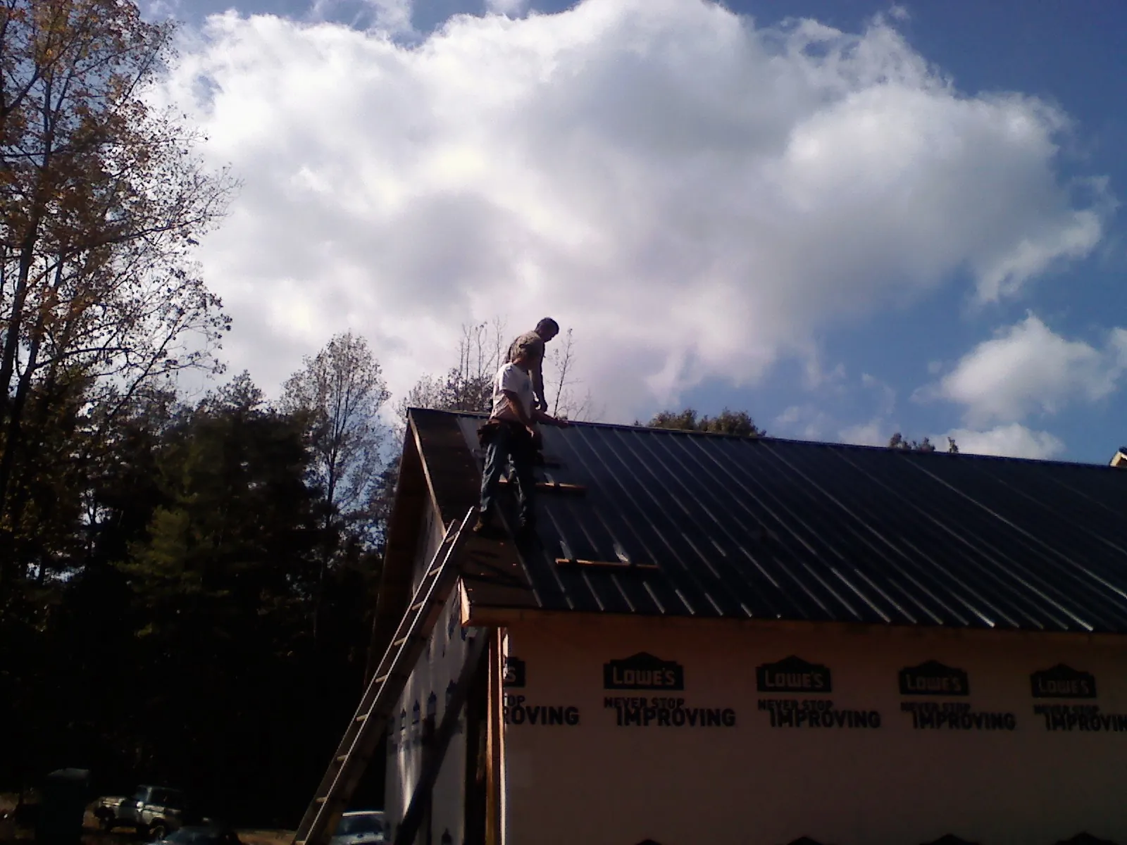 Roofer fastening dark metal panels high against a cloudy sky, from a Roof Inspection job in Spottsville