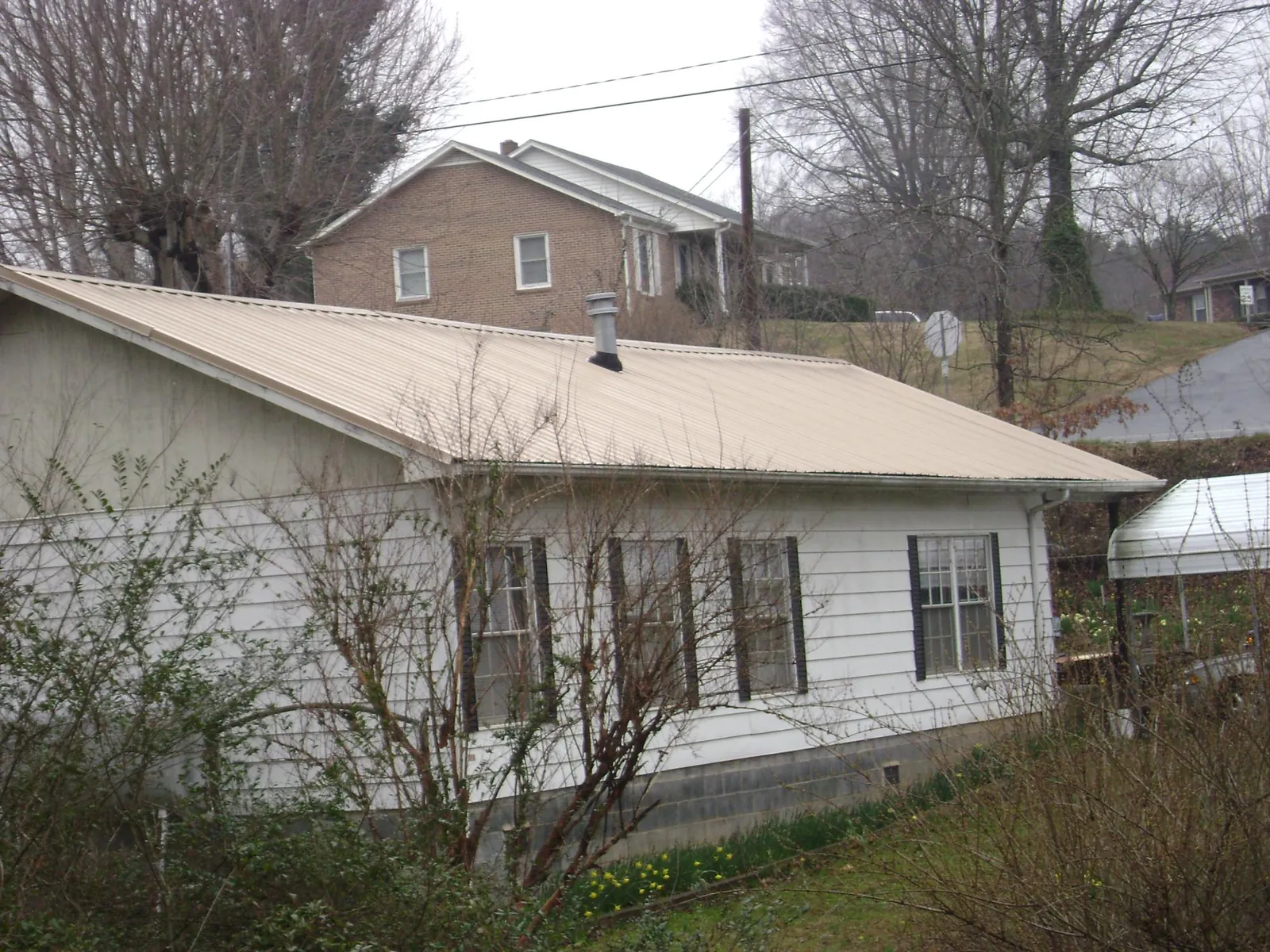 Tan metal roof on a white sided house set into a hillside — Commercial Roofing by Roofing Brothers in Spottsville