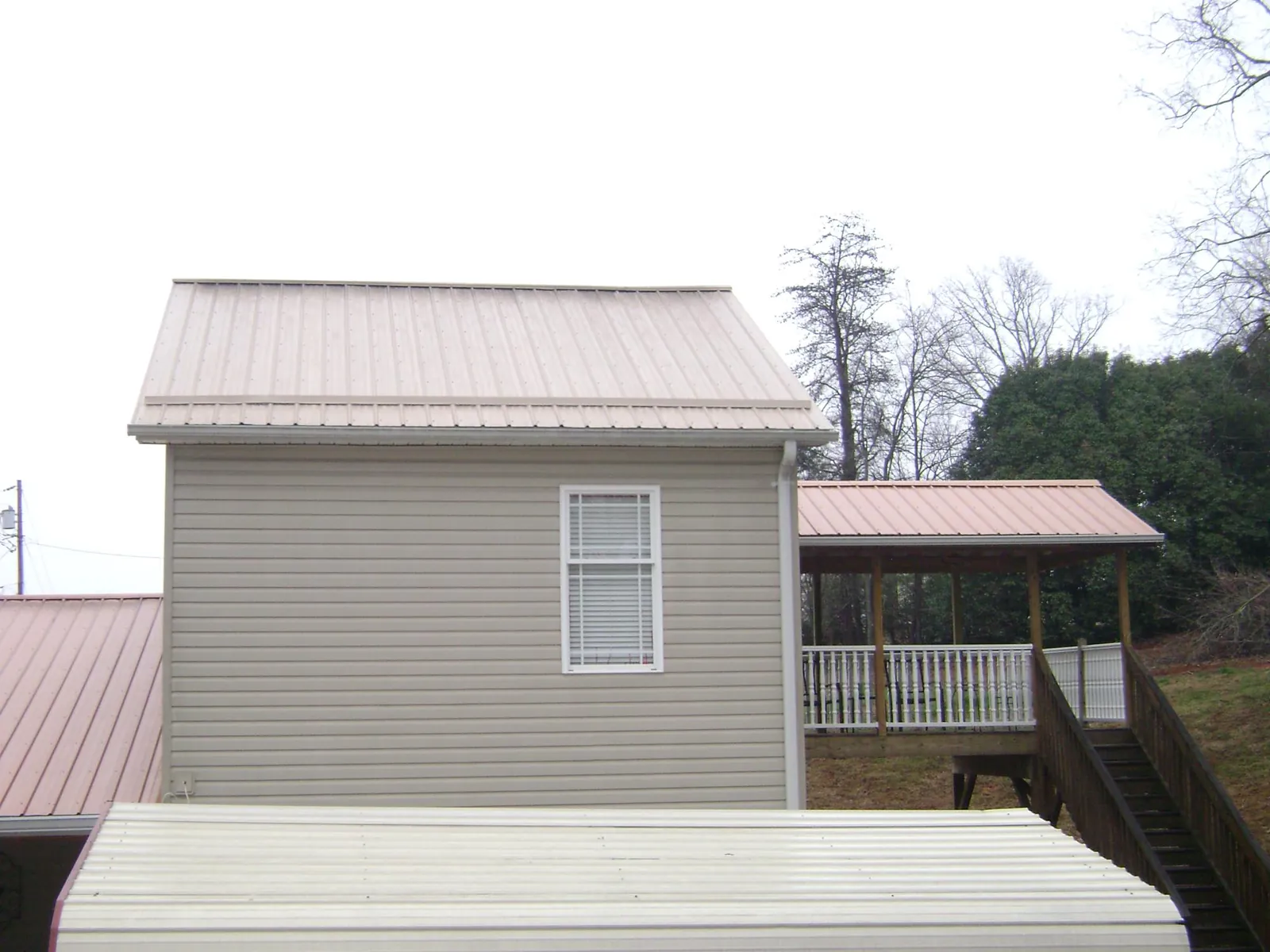 Tan metal roofs on a two story addition and attached porch, from a Roof Replacement job in Spottsville